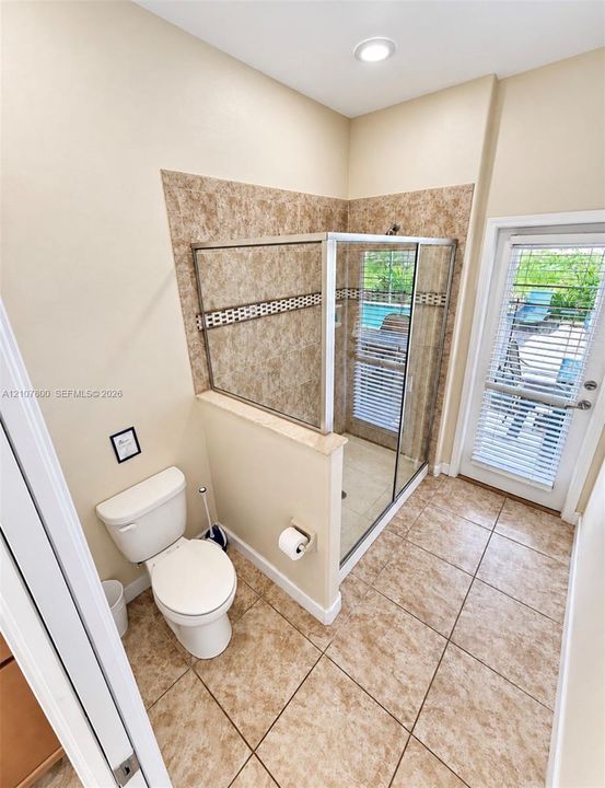 Enclosed glass-door shower featuring tile surround with decorative mosaic accent, ceramic tile flooring, recessed lighting, and a glass-paneled exterior door