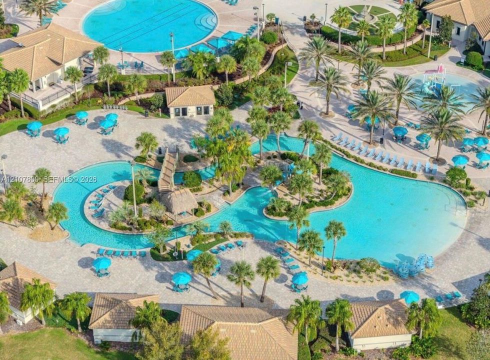 Expansive resort-style aquatic complex featuring a winding lazy river, integrated swimming pools, a pedestrian bridge, and palm tree landscaping