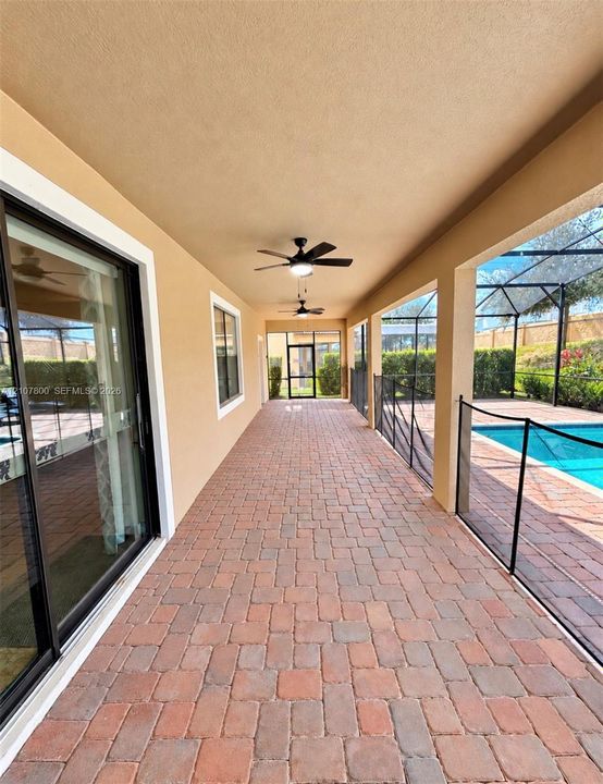 Covered patio featuring brick-paver flooring, dual ceiling fans, sliding glass door access, and a screened-in pool enclosure