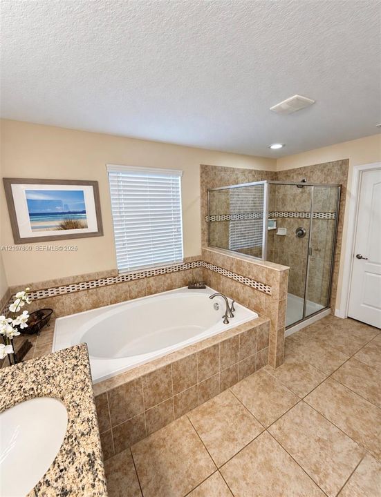 Oval soaking tub with tiled surround, separate glass-enclosed shower, stone-finish countertop, and integrated ceramic sink