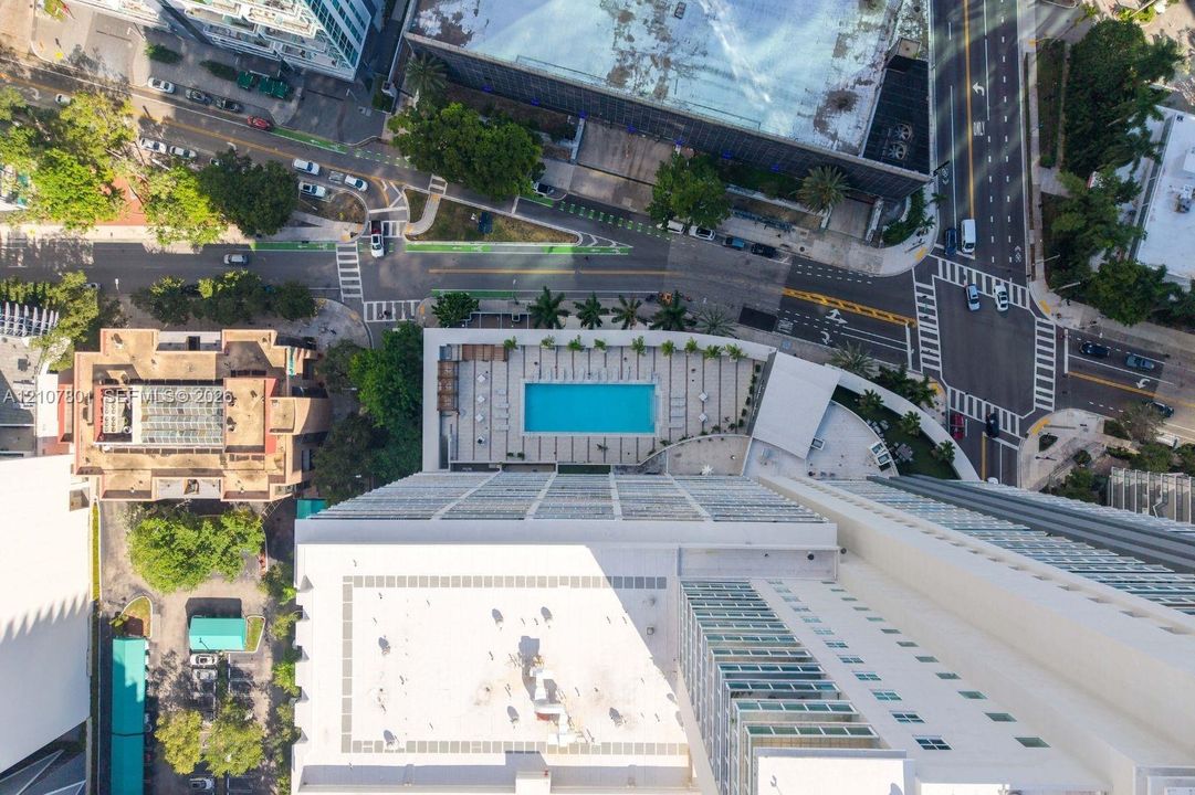 Aerial perspective of high-rise building featuring a rectangular swimming pool, expansive paved deck, and structured urban surroundings