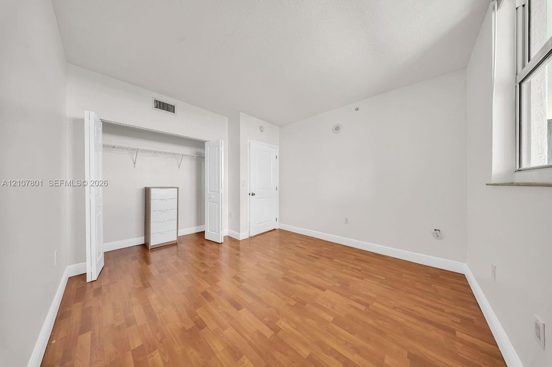 Room featuring wood-finish flooring, a neutral color palette, a window, and a built-in reach-in closet with double doors