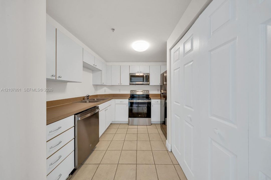 Kitchen featuring white cabinetry, stainless steel appliances, solid-surface countertops, tile flooring, and bi-fold closet doors