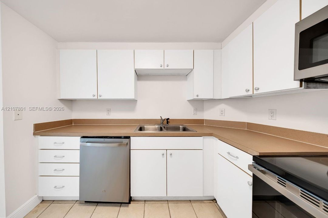Kitchen featuring white cabinetry, solid-surface countertops, dual-basin stainless steel sink, and stainless steel appliances
