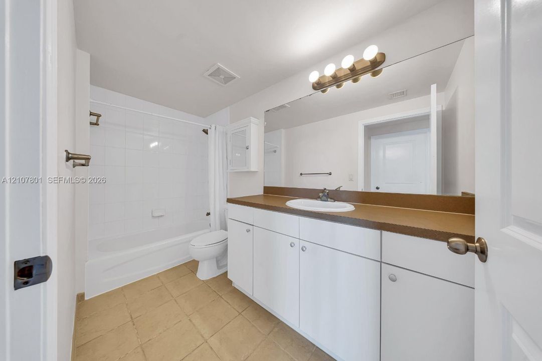 Bathroom featuring a solid-surface countertop, white cabinetry with integrated storage, a full-width wall mirror, and a tub-shower combination with tile surround