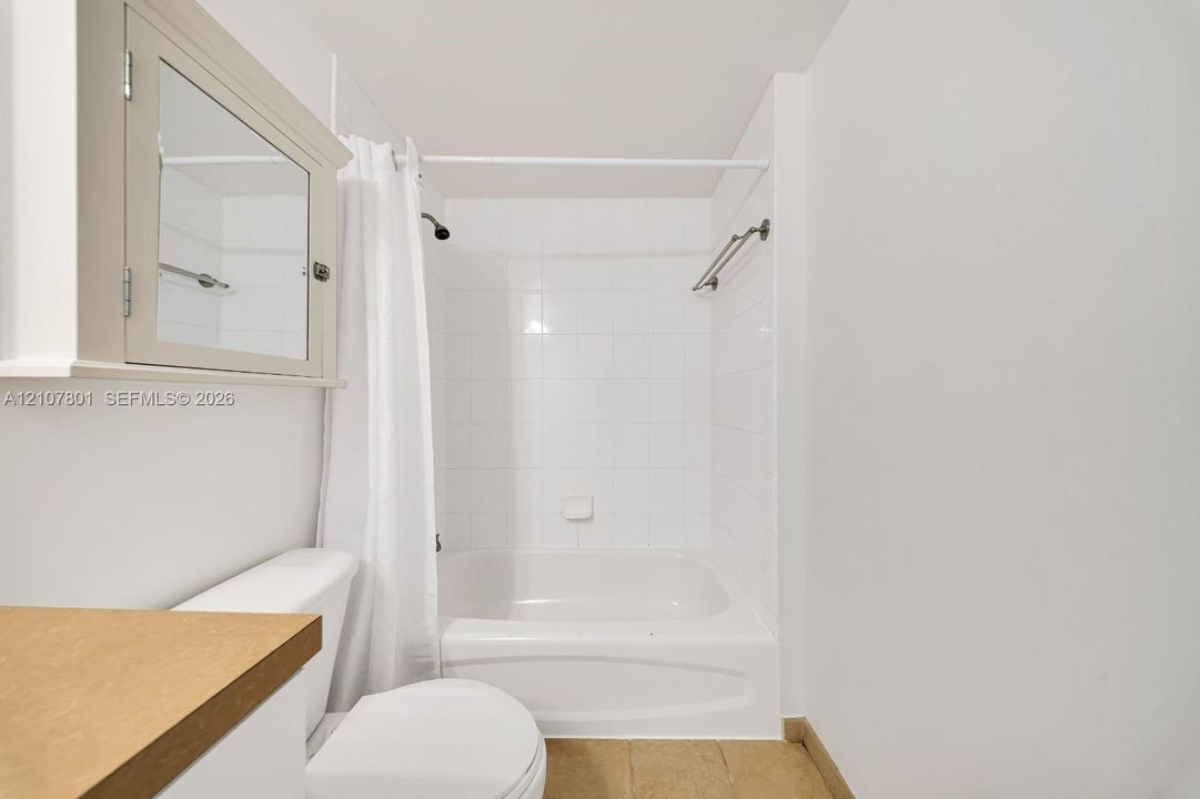 Bathroom featuring a porcelain tub and shower combination with white tile surround, integrated medicine cabinet, and stone-finish countertop