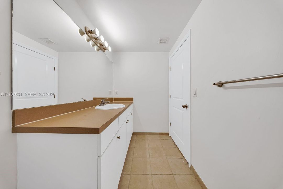 Full-width vanity with solid-surface countertop and integrated sink, expansive wall-to-wall mirror, multi-light fixture, and ceramic tile flooring