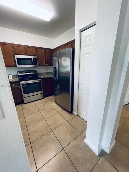 Kitchen featuring dark-toned cabinetry, stone-finish countertops, stainless steel appliances, ceramic tile flooring, and a floor-to-ceiling bi-fold door pantry