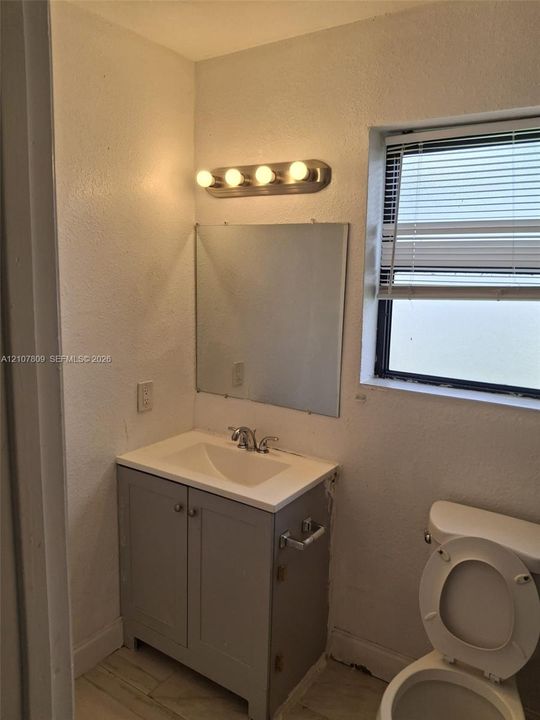 Grey shaker-style vanity with a solid surface countertop, integrated basin, four-light vanity fixture, and wall-mounted mirror