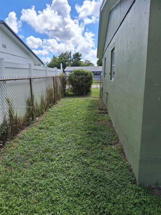 Side exterior featuring a grassy lawn, chain-link perimeter fencing, and a utility spigot