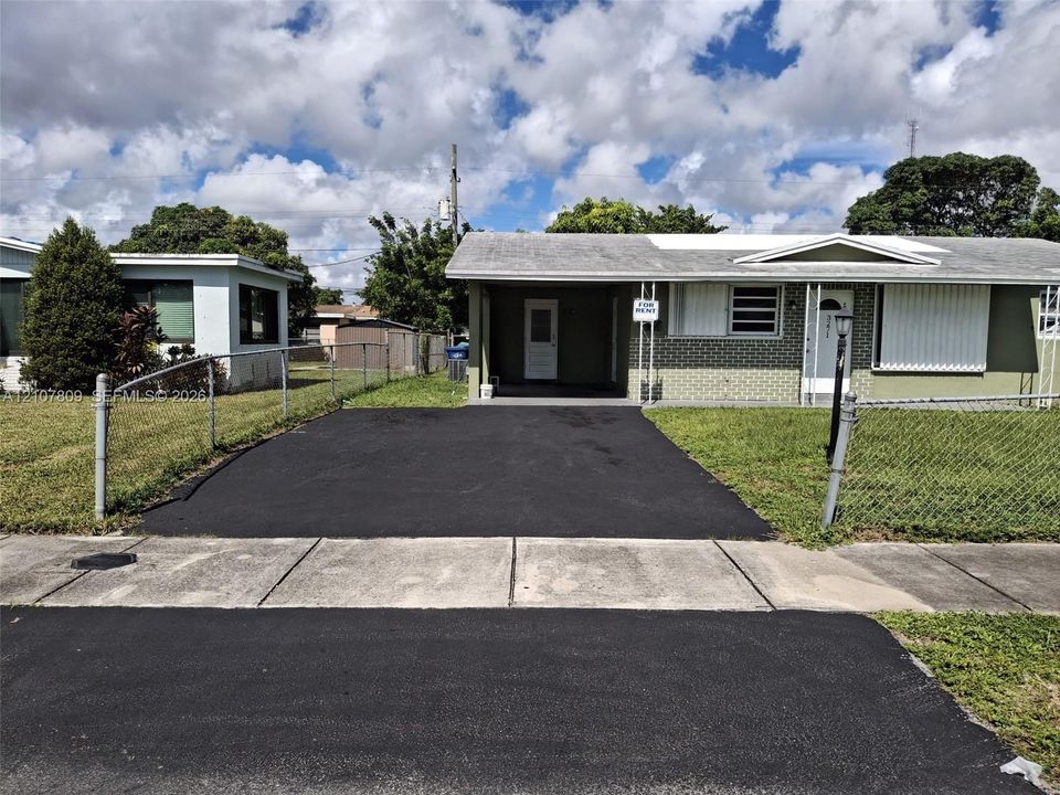 Single-story residence featuring a brick facade, covered carport, chain-link perimeter fencing, and an asphalt driveway