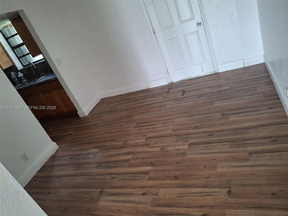 Wood-finish flooring throughout, six-panel interior door, and kitchen featuring wood cabinetry and dark stone-finish countertops