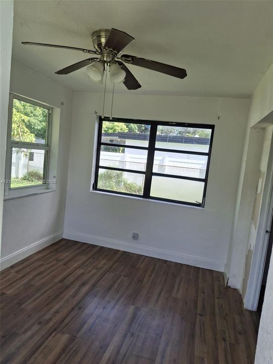 Interior room featuring wood-finish flooring, multi-pane windows with black frames, and a ceiling fan with integrated lighting