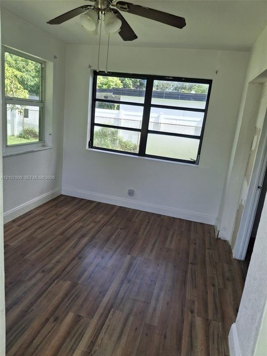 Interior space featuring wood-finish flooring, white walls, black-framed windows, and a ceiling fan with integrated lighting