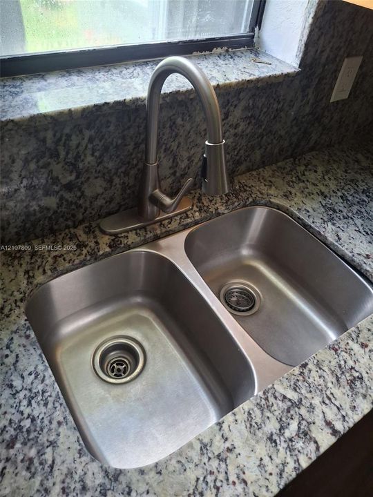 Double-basin stainless steel sink featuring a high-arc pull-down faucet and stone-patterned countertops with a matching backsplash