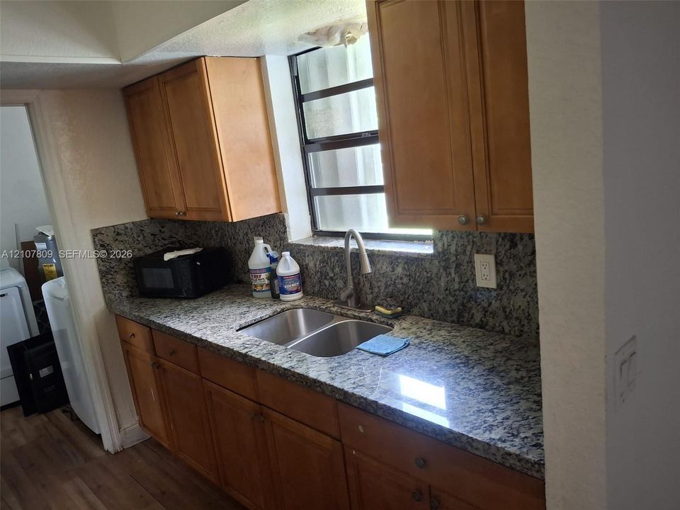 Kitchen featuring wood cabinetry, stone-surface countertops, stone-surface backsplash, stainless steel double-basin sink, and a gooseneck faucet