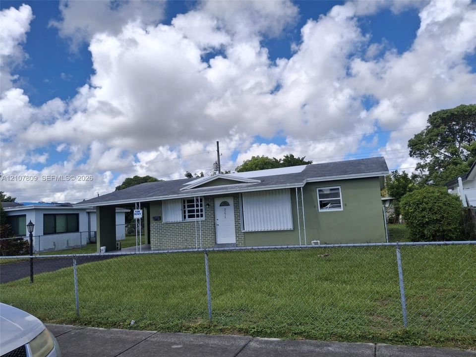 Single-story exterior featuring a masonry facade, covered carport, shingle roof, and exterior hurricane shutters