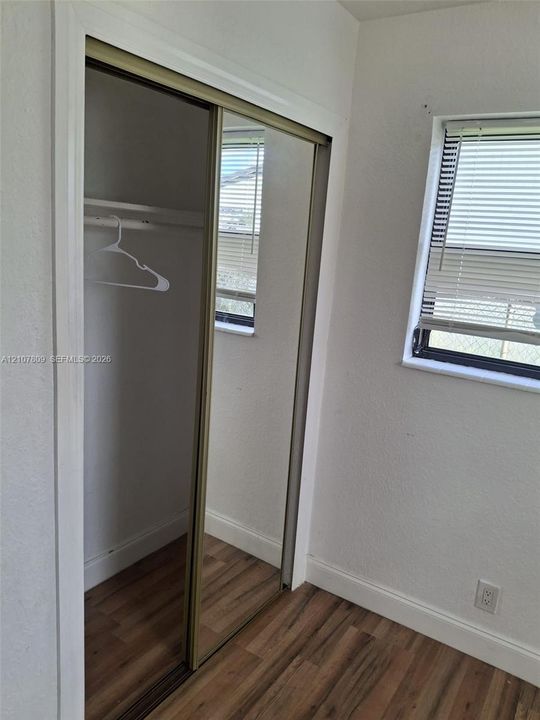 Sliding closet with mirrored panels, wood-finish flooring, and window with adjustable blinds