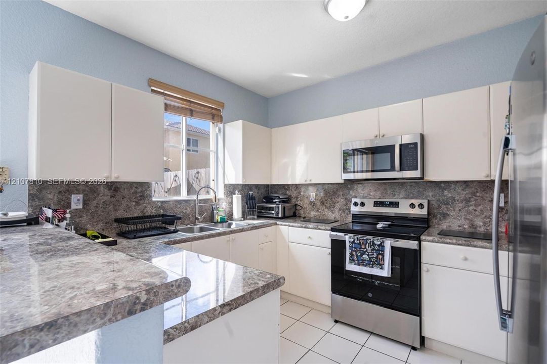 Kitchen featuring white cabinetry, stone-patterned laminate countertops, full-height stone-patterned backsplash, stainless steel appliances, and tile flooring
