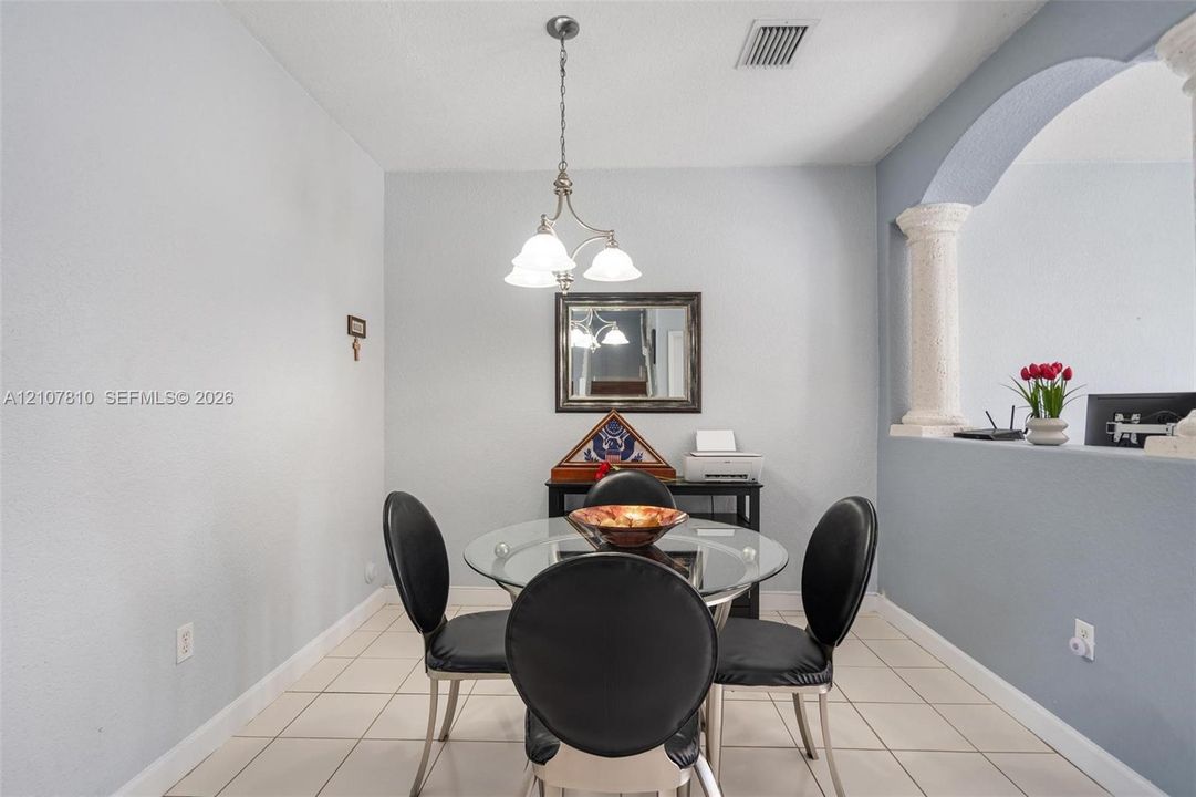 Interior area featuring ceramic tile flooring, a multi-light pendant chandelier, an arched wall cutout, and a decorative column