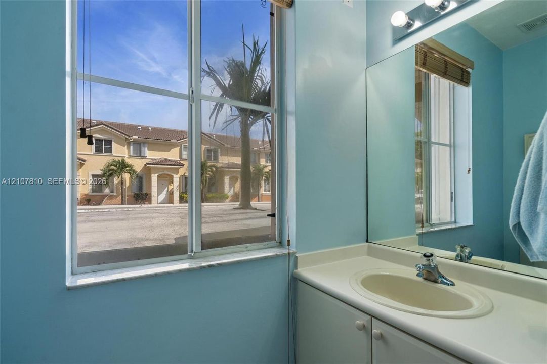 Bathroom vanity featuring an integrated countertop and sink, large wall-mounted mirror, multi-bulb overhead lighting, and a window with exterior exposure