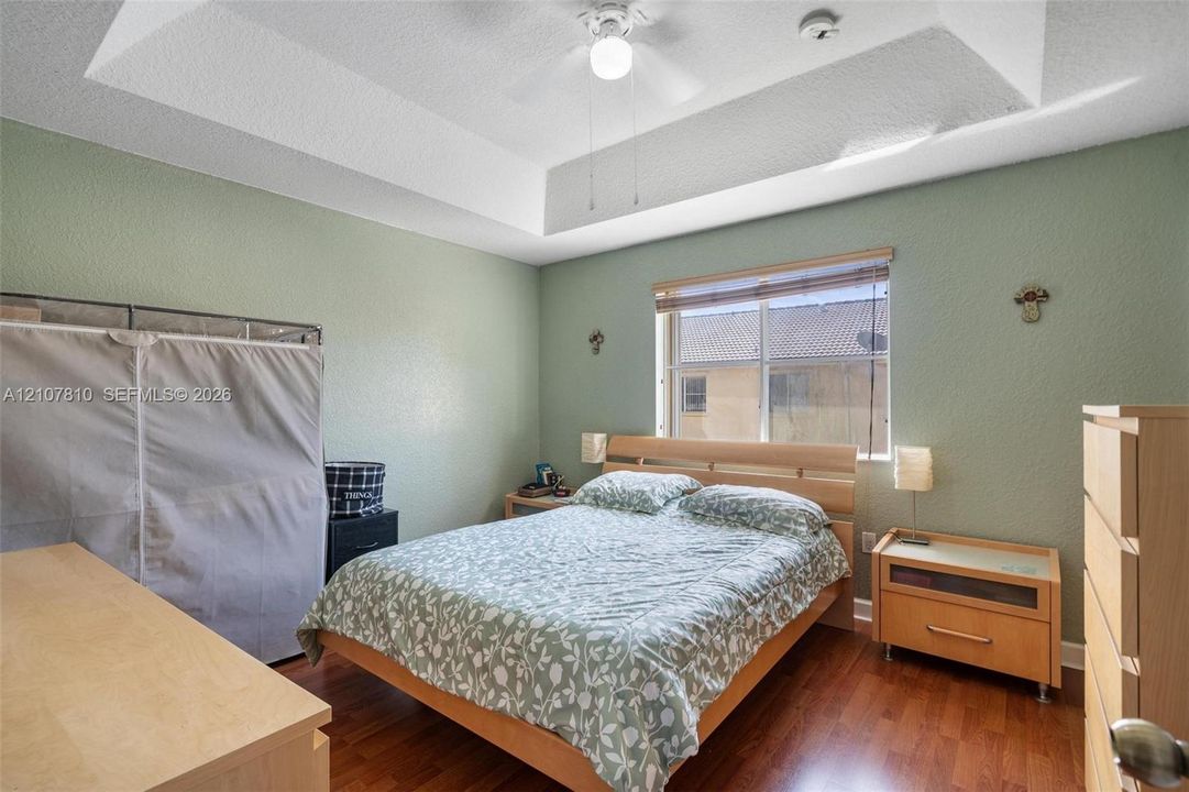 Tray ceiling with centered ceiling fan, wood-finish flooring, and horizontal window with built-in blind