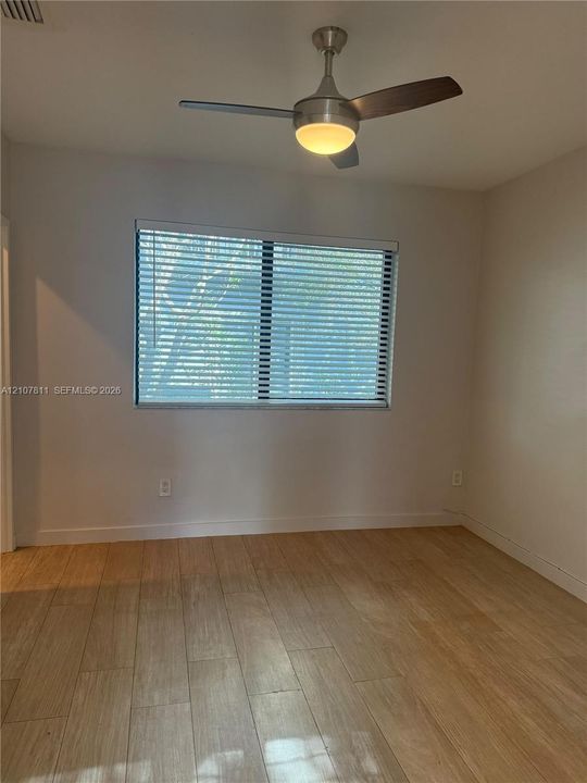 Neutral-toned room featuring wood-finish flooring, a contemporary three-blade ceiling fan with integrated lighting, and a window fitted with horizontal blinds
