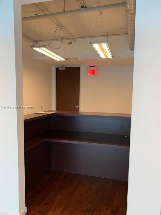 Built-in wooden counter featuring an L-shaped desk surface, exposed ceiling with suspended lighting fixtures, and wood-finish flooring