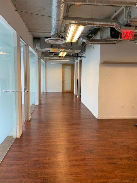 Industrial-style interior featuring wood-finish flooring, exposed ceiling ductwork, glass-panel partition walls, and integrated rectangular light fixtures