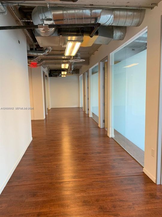 Industrial-style hallway featuring wood-finish flooring, exposed metal ductwork, and glass-partitioned rooms