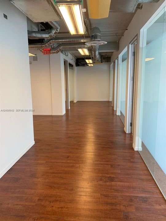 Industrial-style interior featuring wood-finish flooring, exposed ductwork, linear lighting fixtures, and glass-paneled partition walls