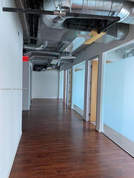 Industrial-style interior featuring exposed ductwork, wood-finish flooring, and floor-to-ceiling glass wall partitions with frosted detailing