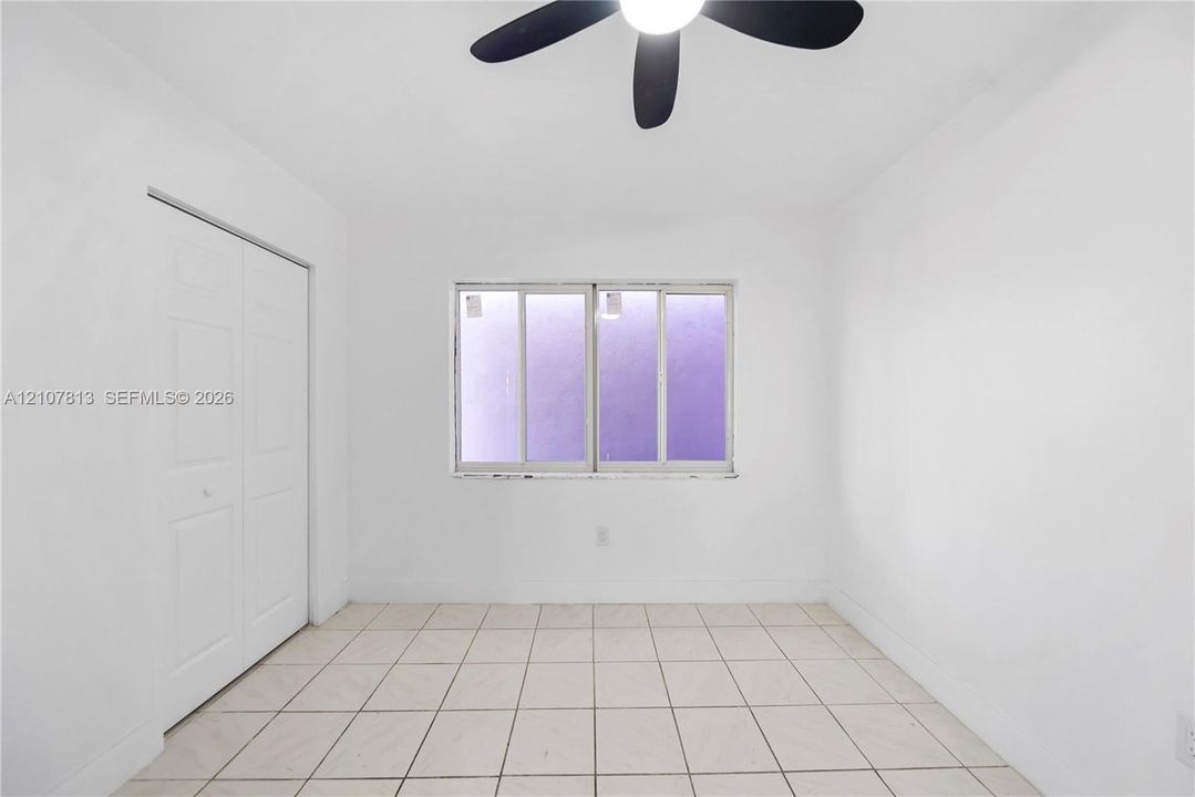 Neutral-toned room featuring large-format ceramic tile flooring, a dual-panel sliding closet, and a multi-blade ceiling fan