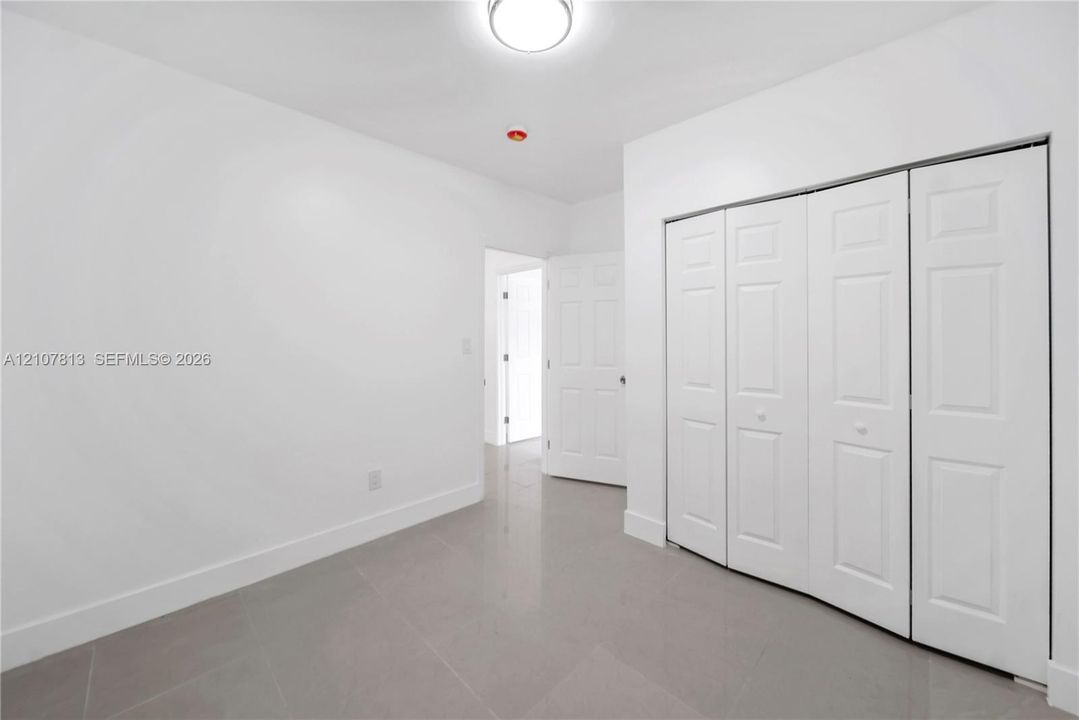 Large-format tile flooring, multi-panel bi-fold closet doors, and flush-mount ceiling lighting