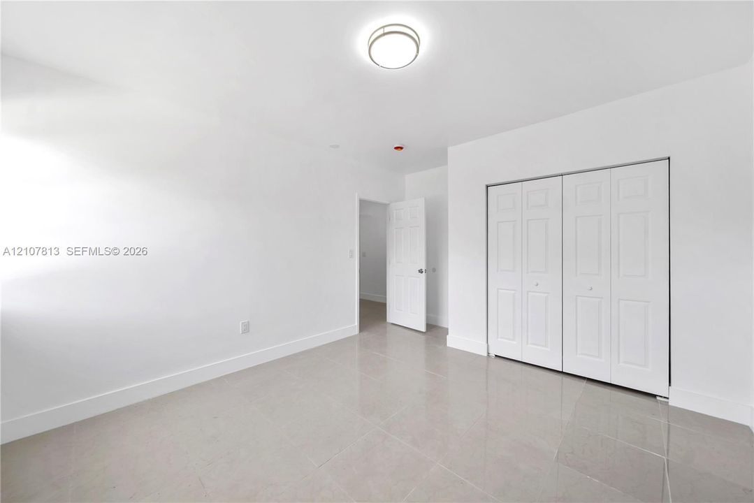 Neutral-toned ceramic tile flooring, crisp white walls, flush-mount dome lighting, and white six-panel folding closet doors