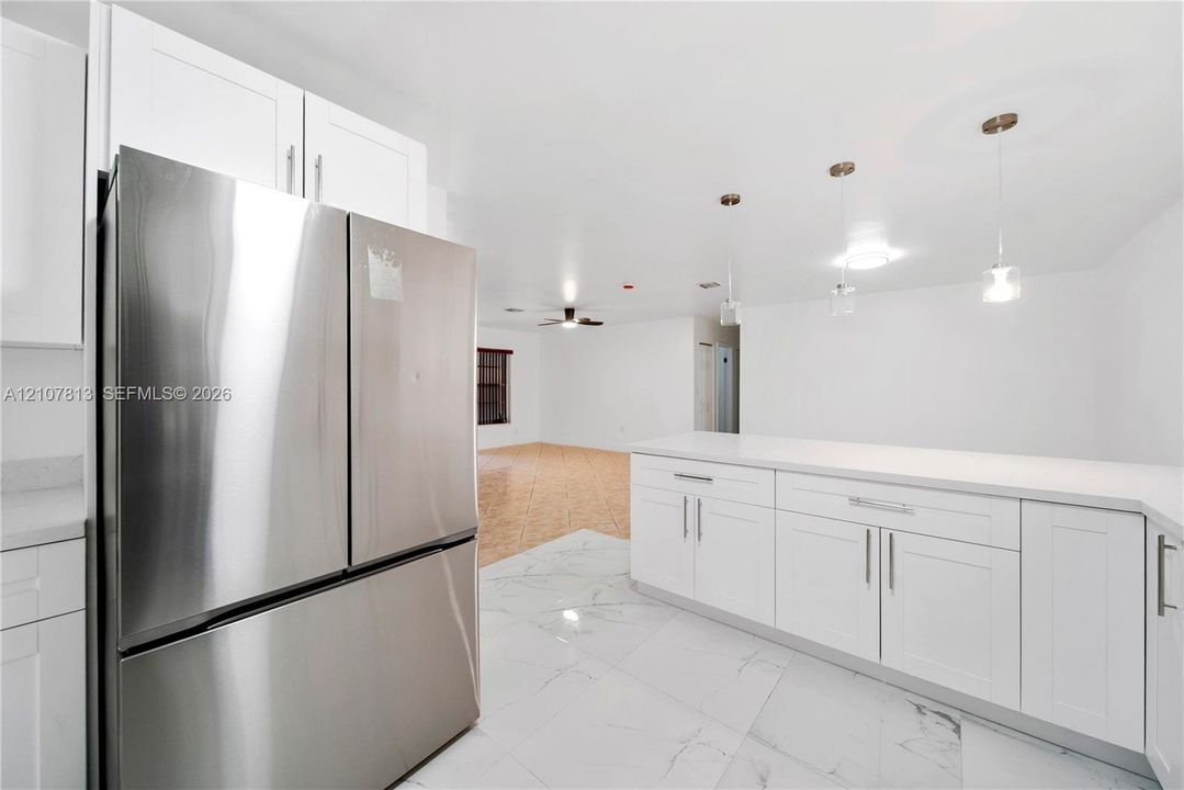 Kitchen featuring white shaker-style cabinetry, stainless steel refrigerator, white countertops, large-format tile flooring, and three glass pendant lights