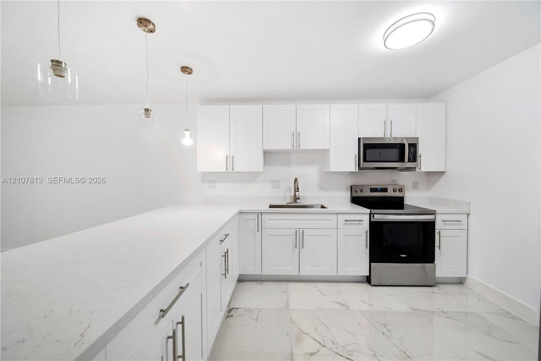 Kitchen featuring white cabinetry, quartz countertops, stainless steel appliances, pendant lighting, and large-format tile flooring