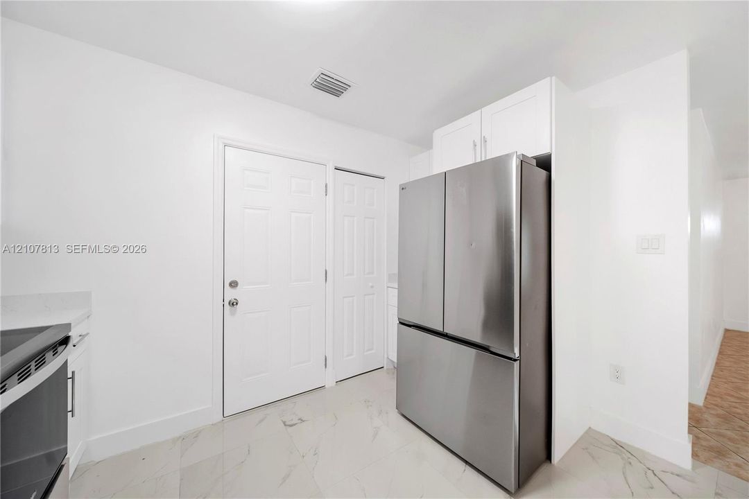Stainless steel French-door refrigerator, white shaker-style cabinetry, large-format tile flooring, and solid-core interior doors