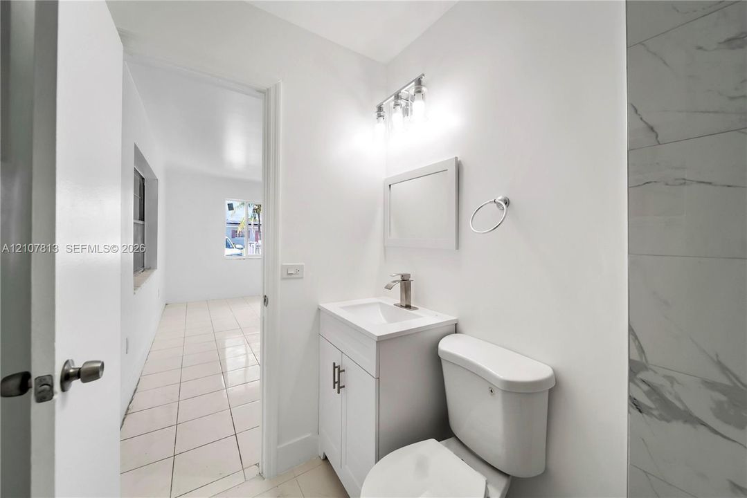 Bathroom featuring a white vanity cabinet, rectangular sink, chrome single-handle faucet, three-light fixture, and light-toned tile flooring