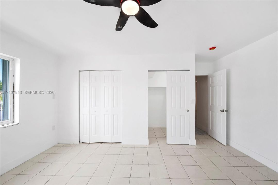 Neutral-toned ceramic tile flooring, ceiling-mounted fan with integrated lighting, dual bi-fold closet doors, and interior paneled doors