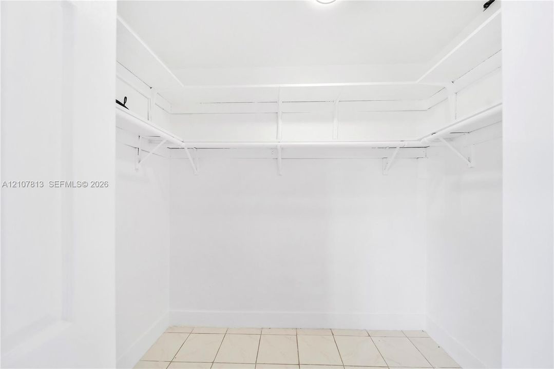 Walk-in closet featuring white walls, built-in shelving, integrated clothing rods, and tile flooring