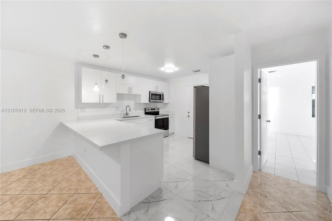 Kitchen featuring white shaker-style cabinetry, a quartz countertop island with pendant lighting, stainless steel appliances, and large-format tile flooring