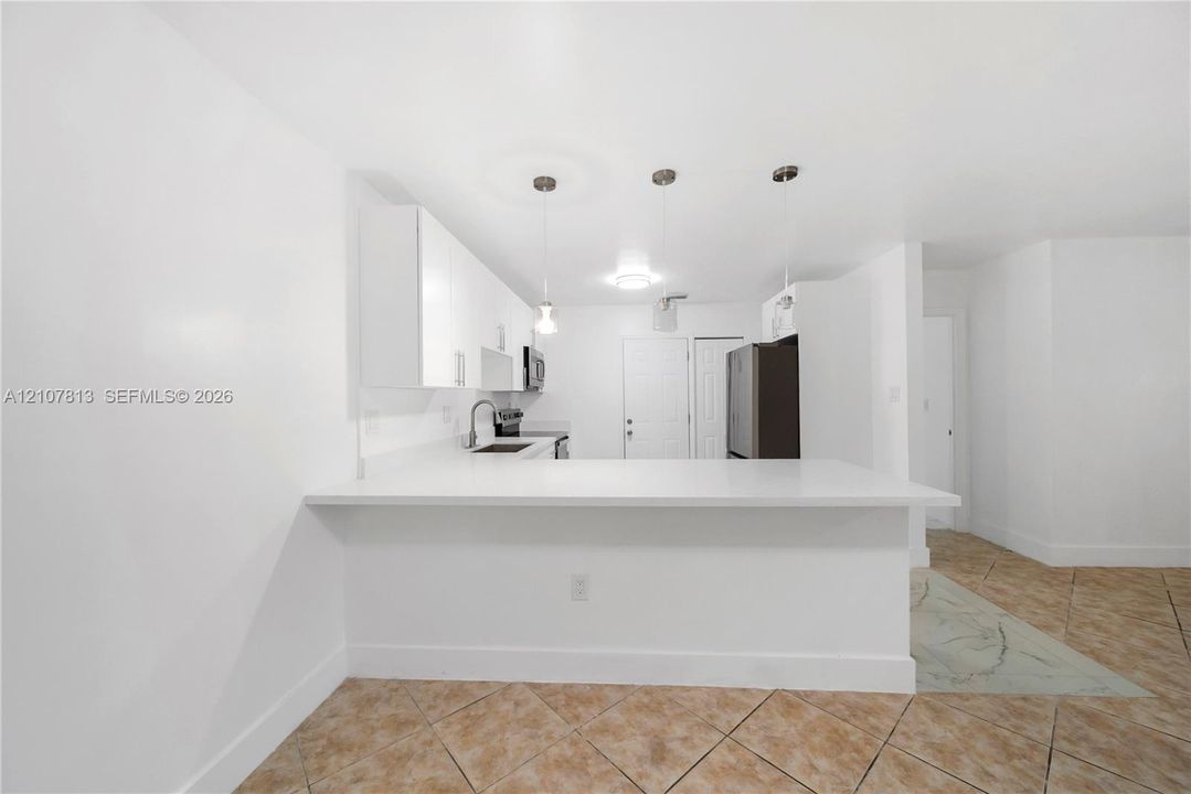 Kitchen featuring white flat-panel cabinetry, light-toned stone countertops, a breakfast bar, stone-finish tile flooring, and triple pendant lighting