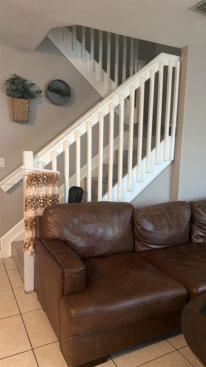 Staircase featuring white balusters, a wooden handrail, and ceramic tile flooring