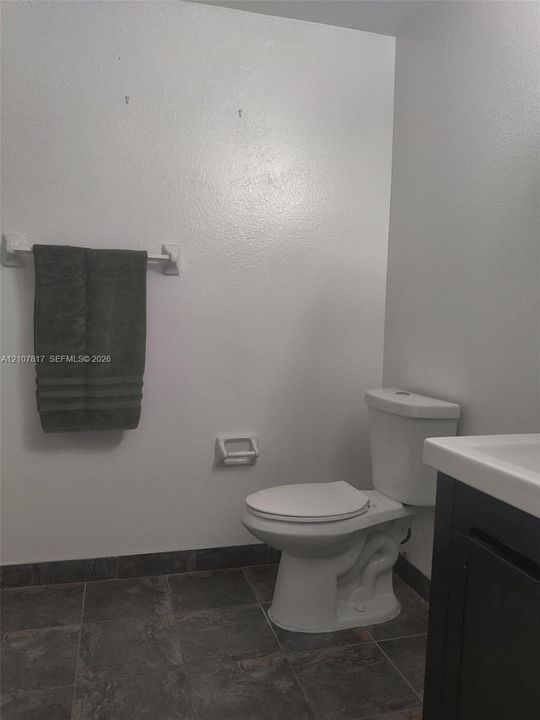 Dark-toned vanity with a rectangular sink, white commode, and dark tile flooring