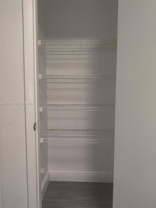 Storage closet featuring four tiers of white wire shelving and wood-finish flooring