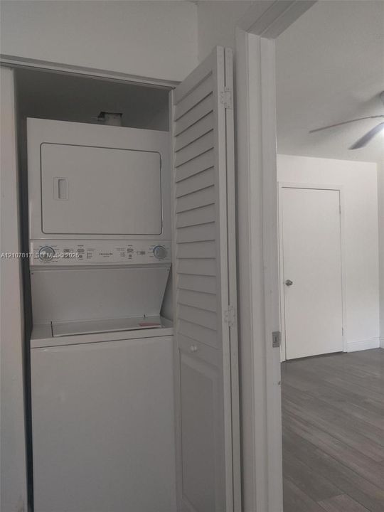 Laundry closet featuring a white stacked washer and dryer unit enclosed by louvered bi-fold doors