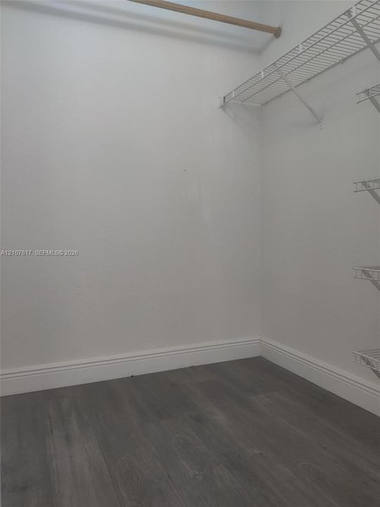 Storage area featuring wood-finish flooring and white shelving with an integrated hanging rod