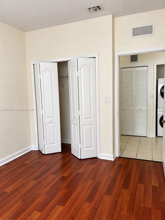Room featuring wood-finish flooring, dual bi-fold closet doors, and tile flooring within the secondary space