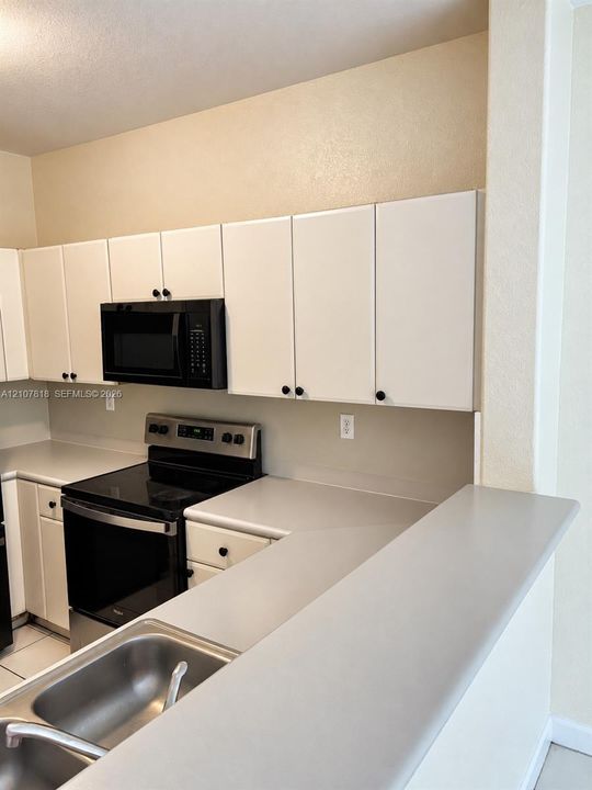 Kitchen featuring white cabinetry with dark hardware, solid-surface countertops, dual-basin stainless steel sink, and black appliances including a built-in microwave and range